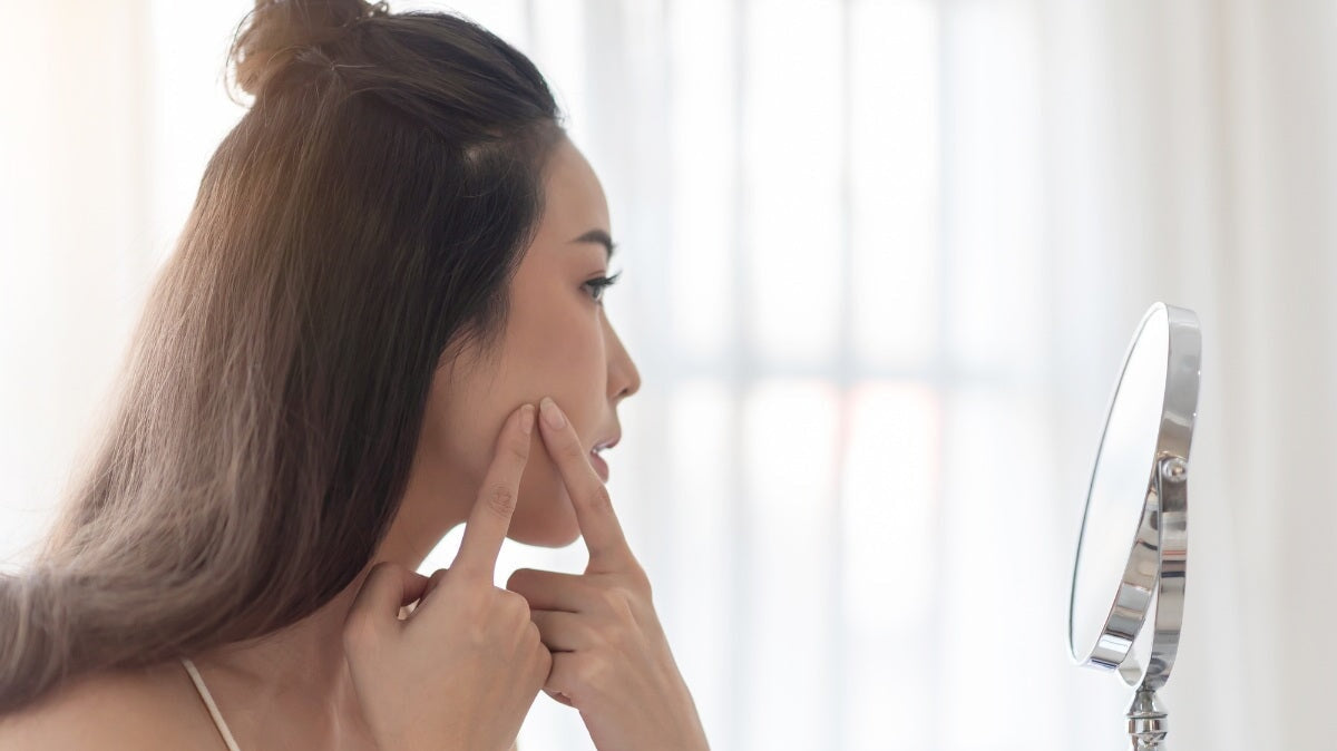 une femme inquiète regardant son acné dans le miroir