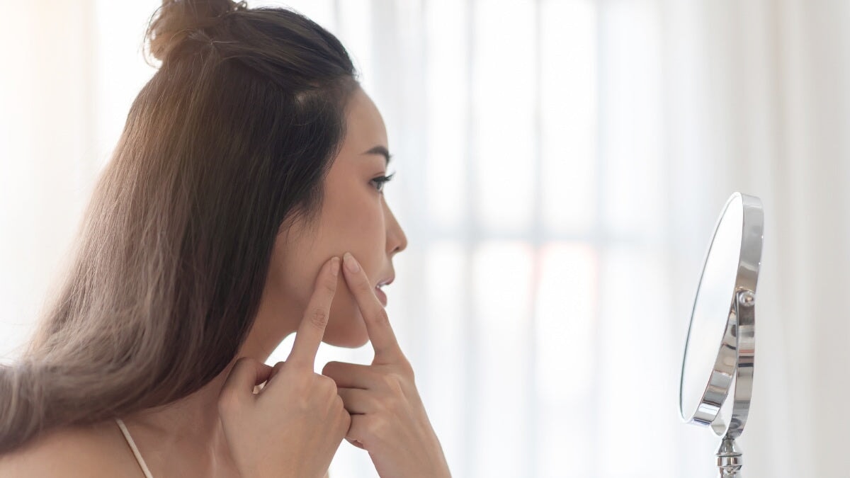 une femme inquiète regardant son acné dans le miroir